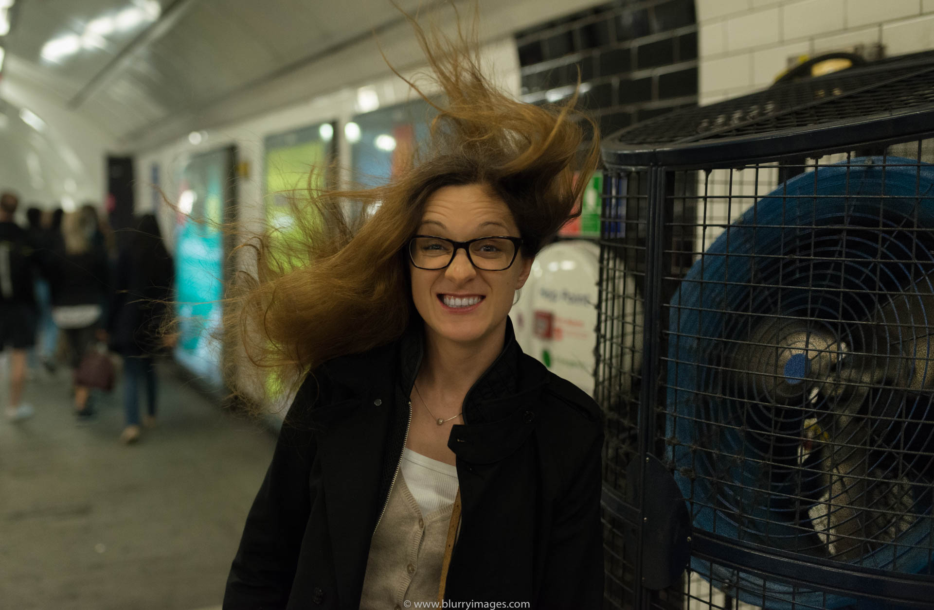 tube station, people, street, woman, tube, fan, real people, London - England, 2016, brown hear, adults only, casual clothing, colour image, portrait, long hair, young adult, headshot, Europe, England, black jacket, brown hair, blue fan, curly hair, blowing, indoors, 2016, Tube station, blurry background