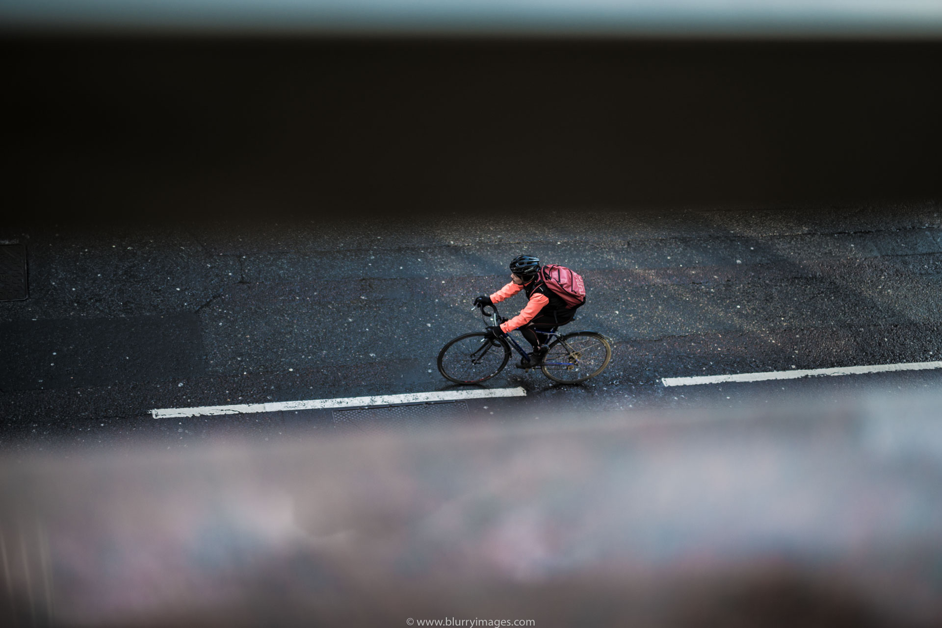 2016, man on bike, riding bike, black jacket, orange jacket, black bike, black fence, through the fence, red backpack,