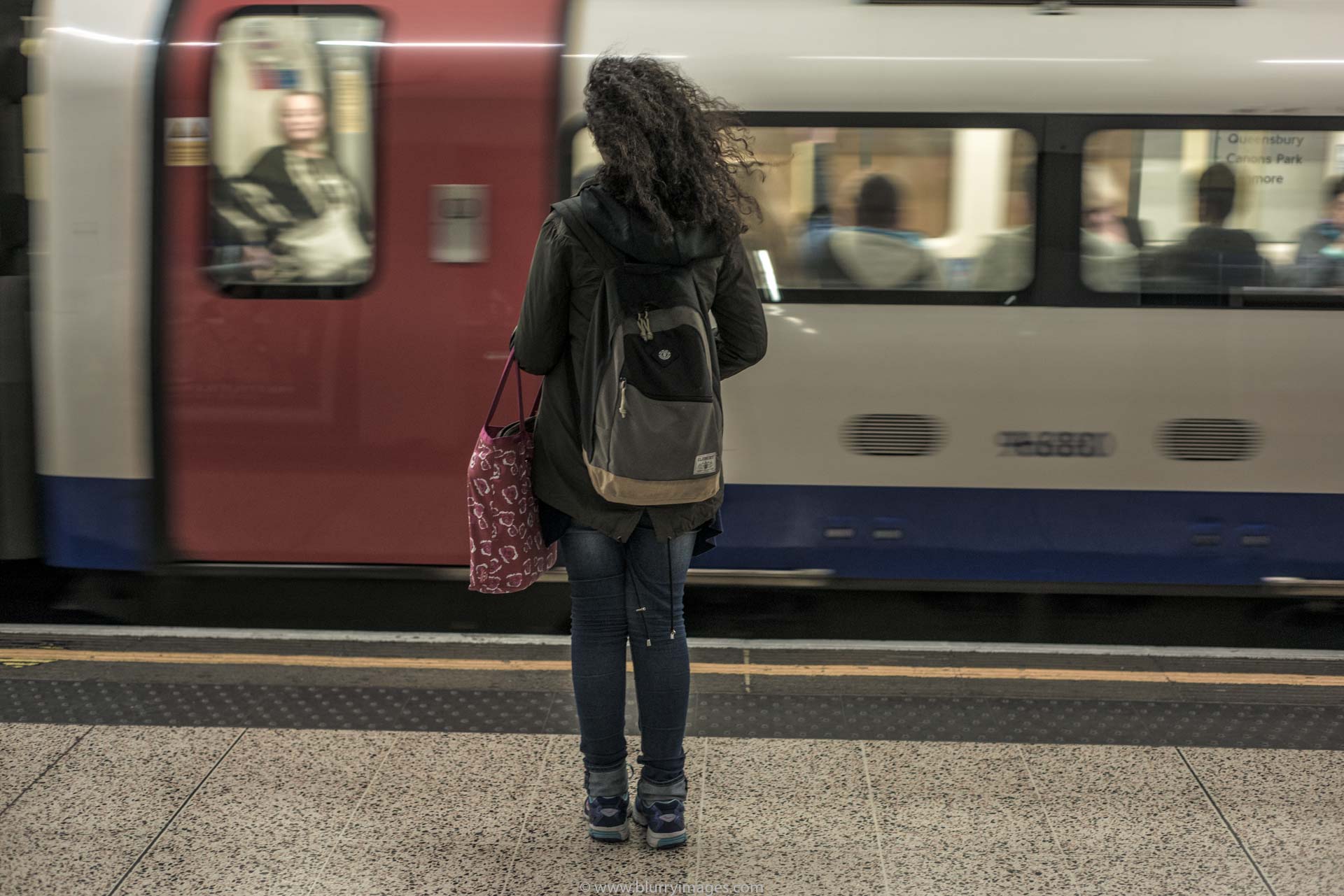 London tube, tube station, metro station, waiting for a train, red bag, blue jeans, trousers, coach, windows, blurry pictures, grey coat, grey jacket, black hair, dark hair, woman's hair, 2016, backpack