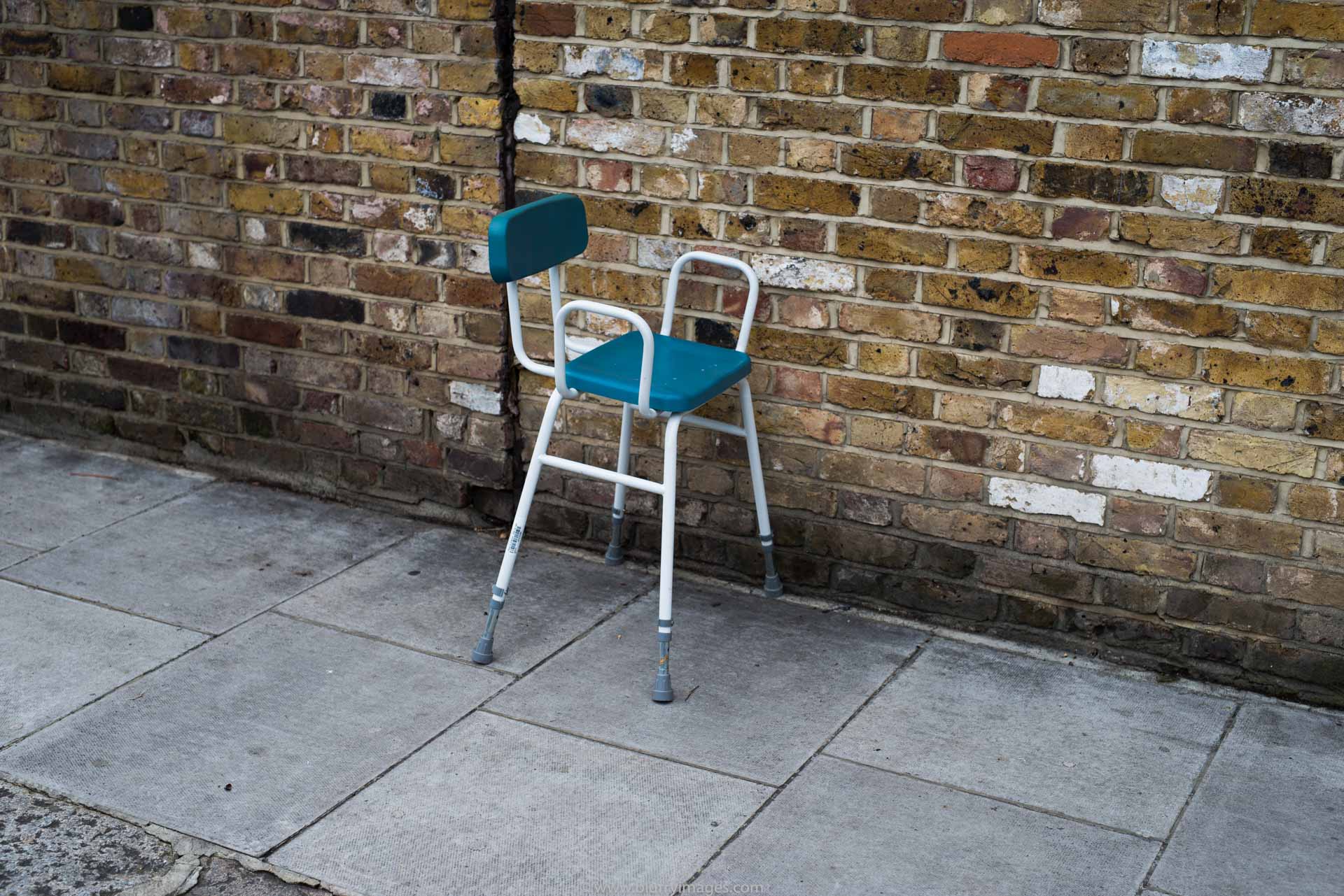 chair, 2015, no people, colour image, horizontal, outdoor furniture, photography, wall - building feature, blue chair, white arm, chair on a pavement, red brick, outdoors,