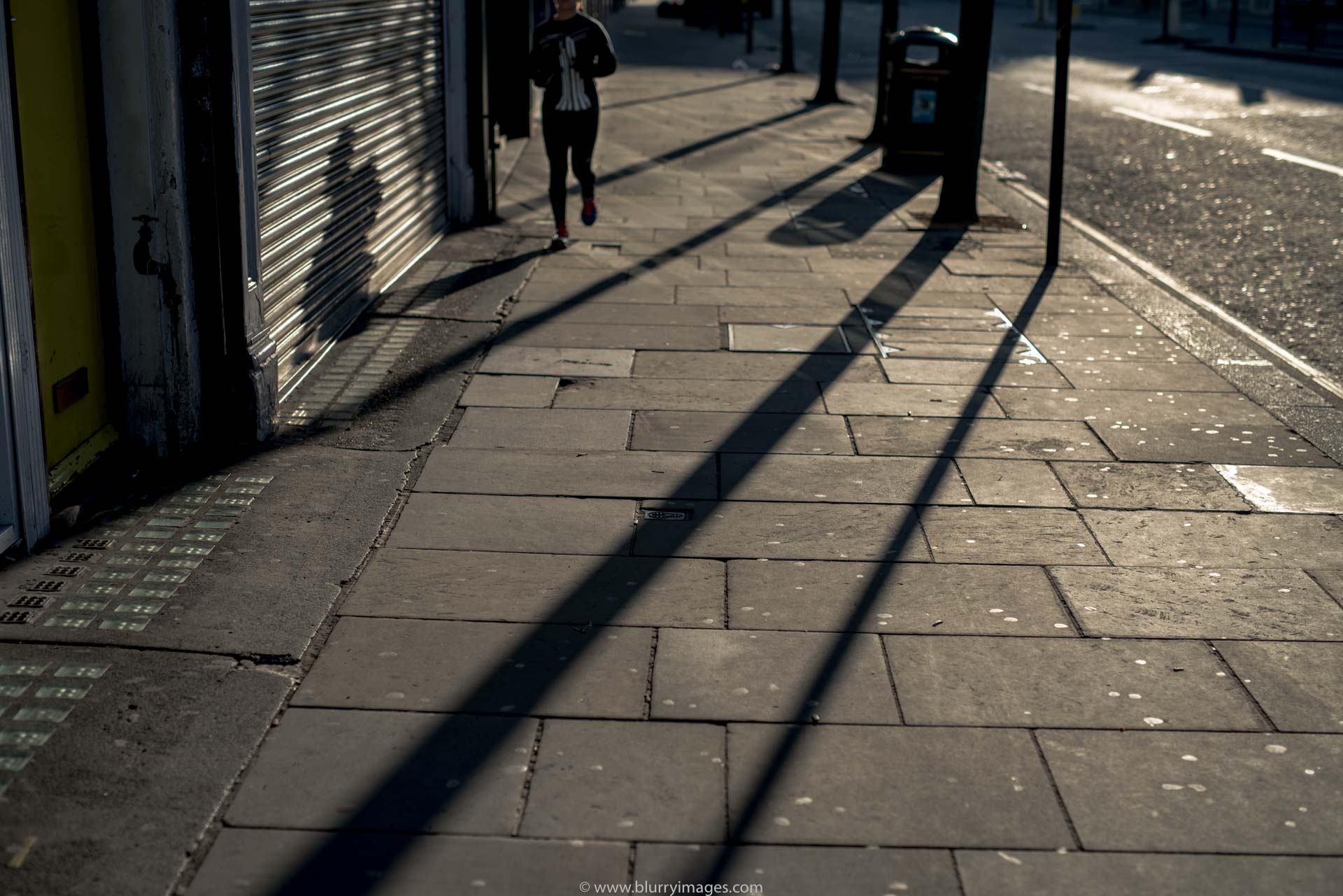 contrast, running woman, sun on pavement, pavement, sidewalk, rubbish, shop display,